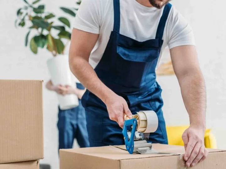 A mover taping a cardboard box shut with a tape gun